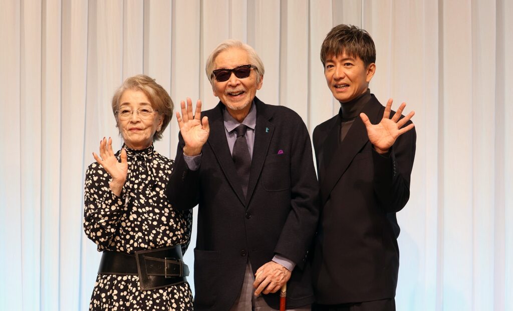 Publicity photo for the 2025 Japanese film "TOKYOタクシー (Tokyo Taxi)", with senior actors including a woman in floral print and an older man in sunglasses, smiling and waving at a promotional event.