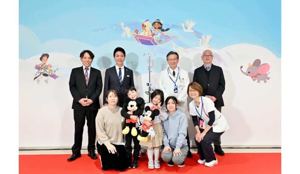 2月2日（月）に開催した、壁紙お披露目セレモニーの様子 後列左から：ディズニー兼田、高島福岡市長、楠原院長、福島 NPO 専務理事 前列左から：治療を受けているおこさまとご家族、吉冨看護部長